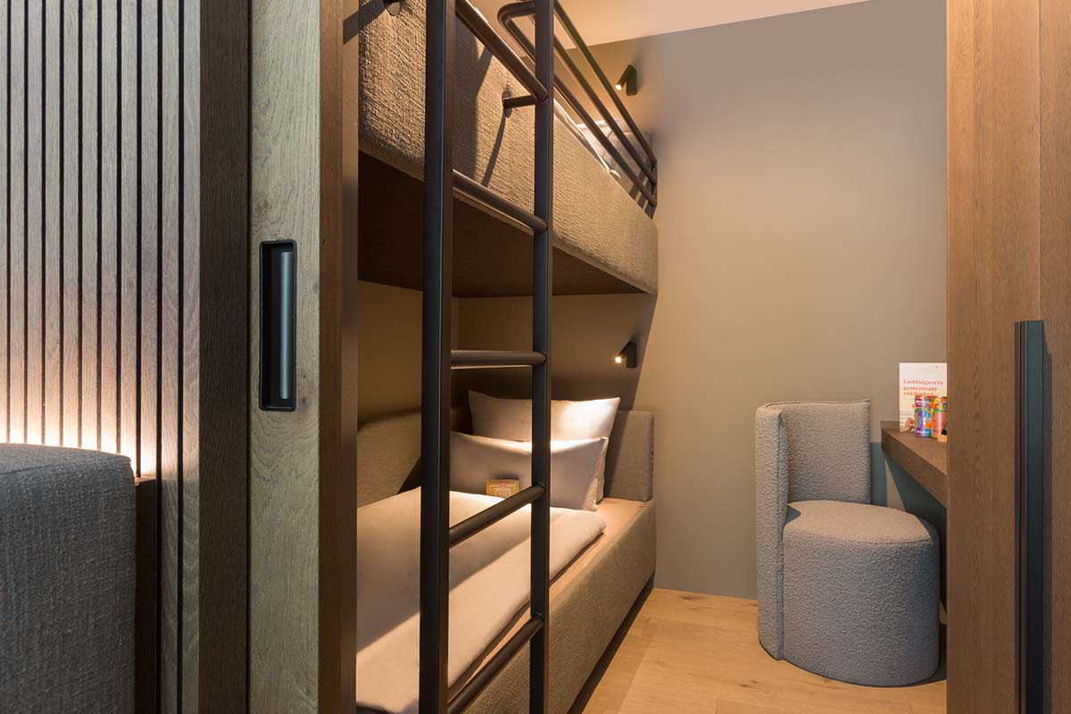 Modernes Hochbett im gemütlichen Hotelzimmer des TRIFORÊT alpin.resorts mit Leseecke.