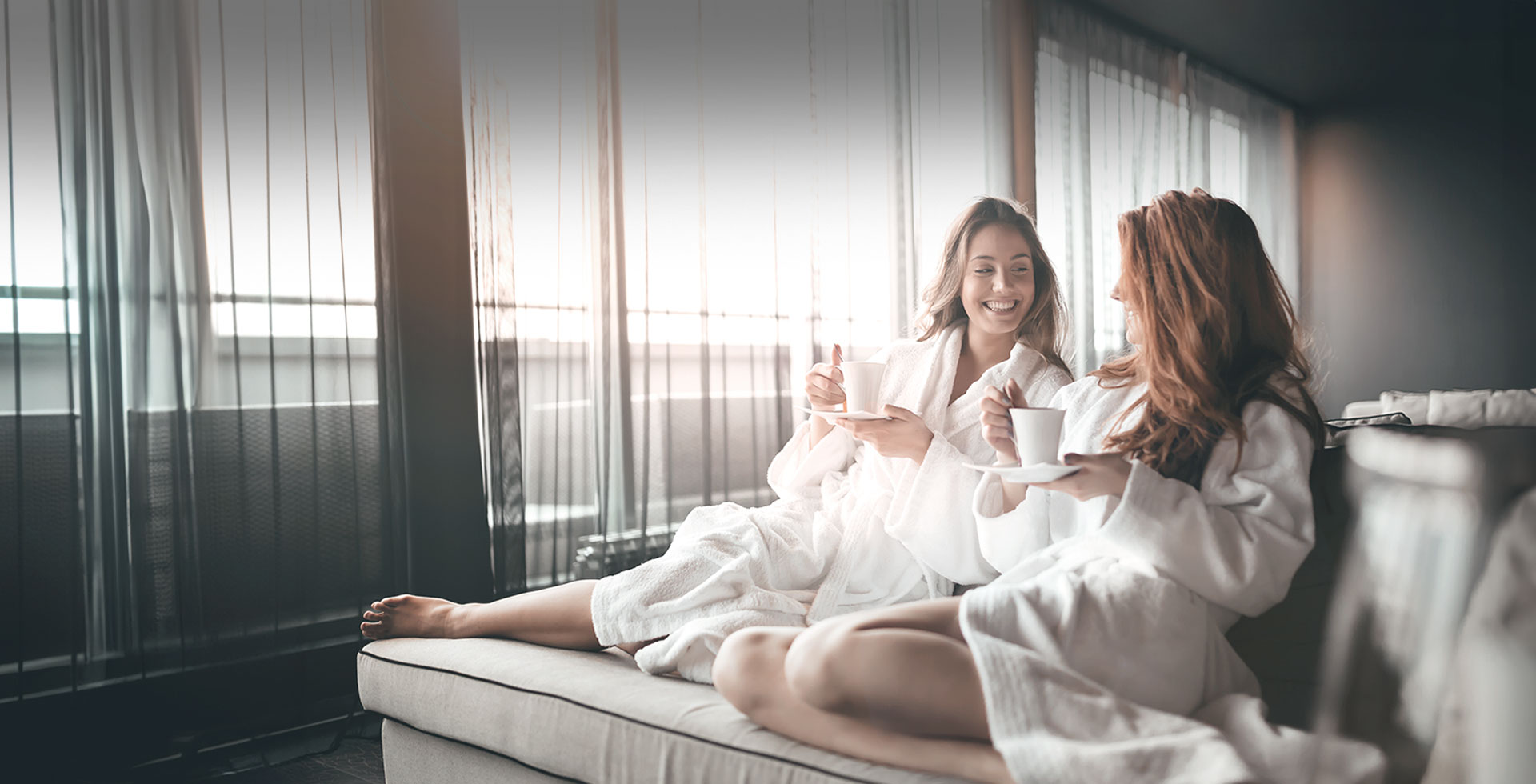 Zwei Freundinnen im Bademantel genießen Kaffee im stilvollen Hotelzimmer des TRIFORÊT alpin.resort.