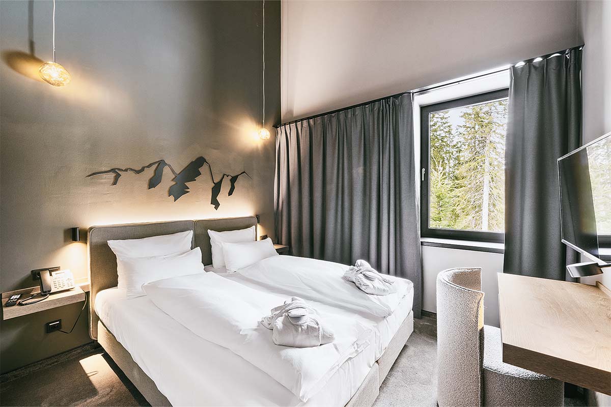 Cosy double bed in the bright bedroom of the "Kleiner Priel" suite at the Triforêt alpin.resort in Hinterstoder.