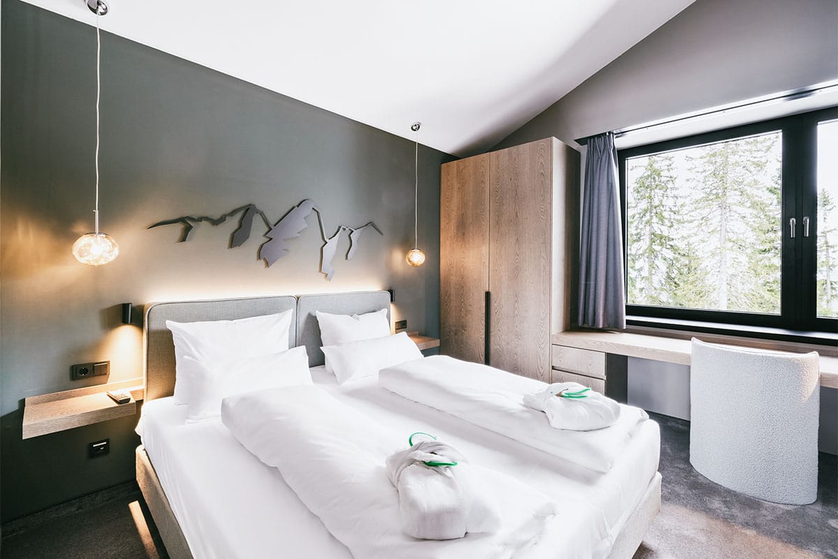 Cosy double bed in one of the three bright bedrooms of the Deluxe Suite at the Triforêt alpin.resort in Hinterstoder.