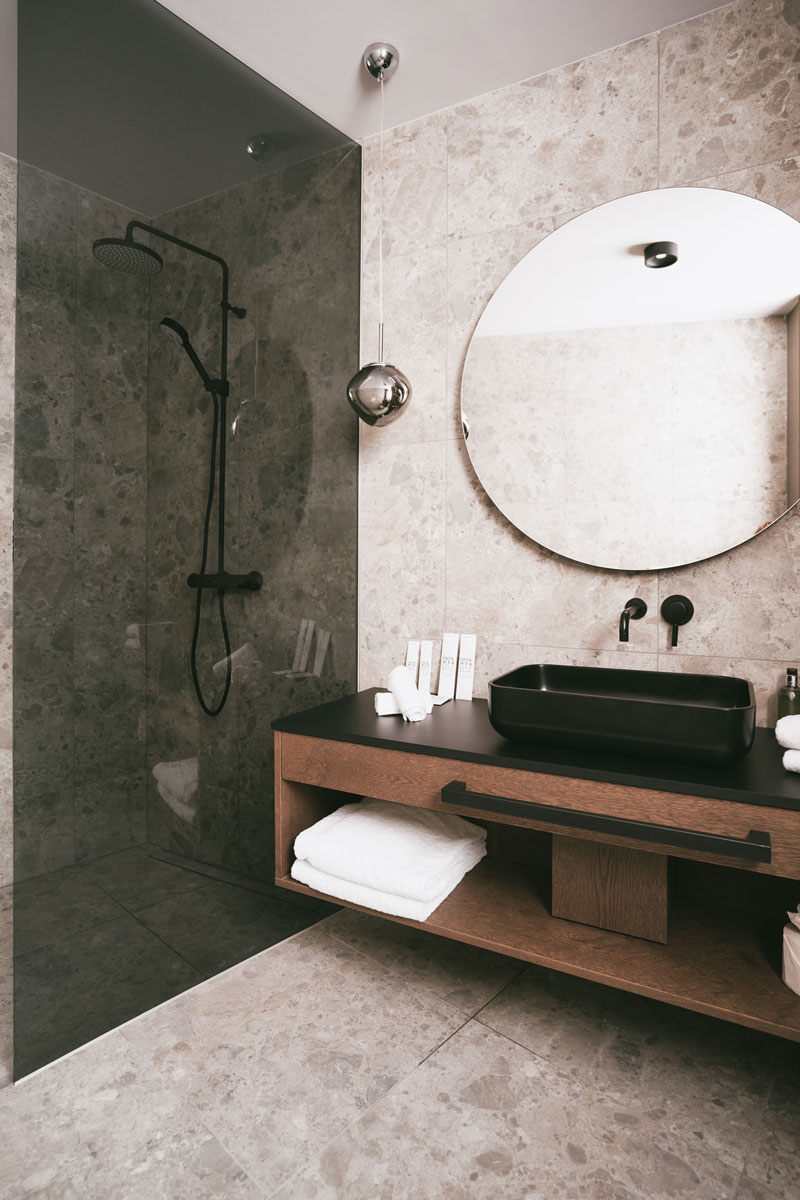 Spacious walk-in shower and washstand with mirror in the bathroom of the Deluxe Penthouse Suite at the TRIFORÊT alpin.resort.