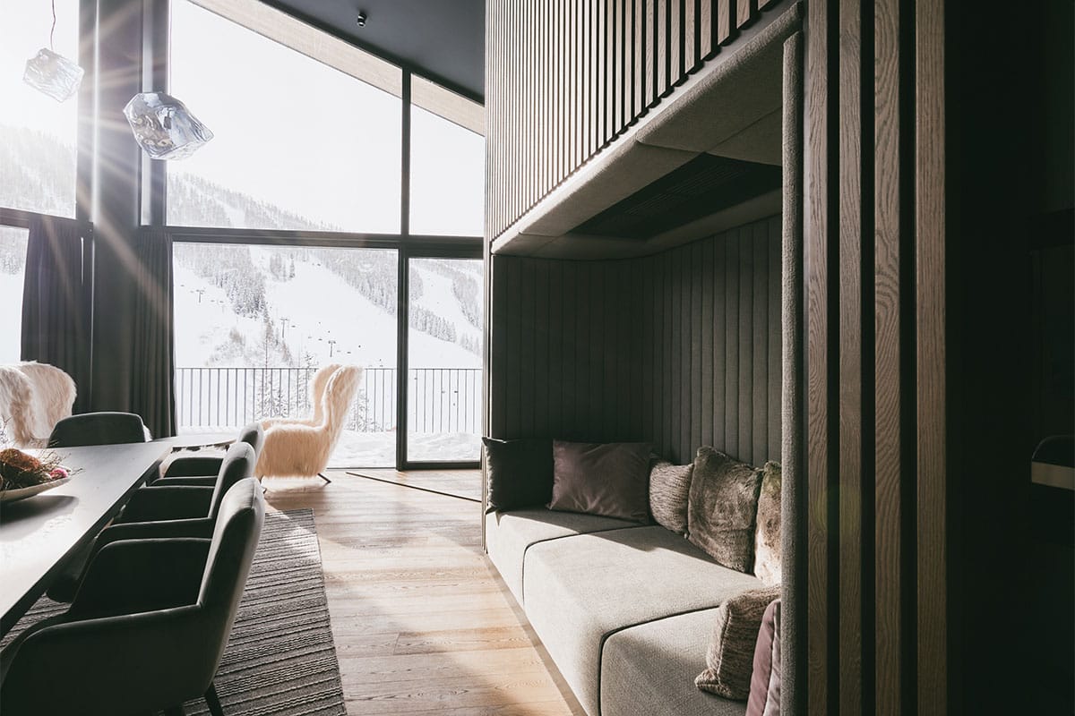 Sunlight shines through the panoramic window of the living area in the Deluxe Penthouse Suite at the TRIFORÊT alpin.resort.