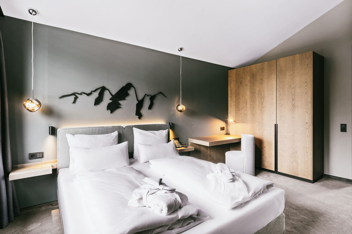 Cosy double bed in one of the two bright bedrooms of the Deluxe Suite "Hoesskogel" at the TRIFORÊT alpin.resort.