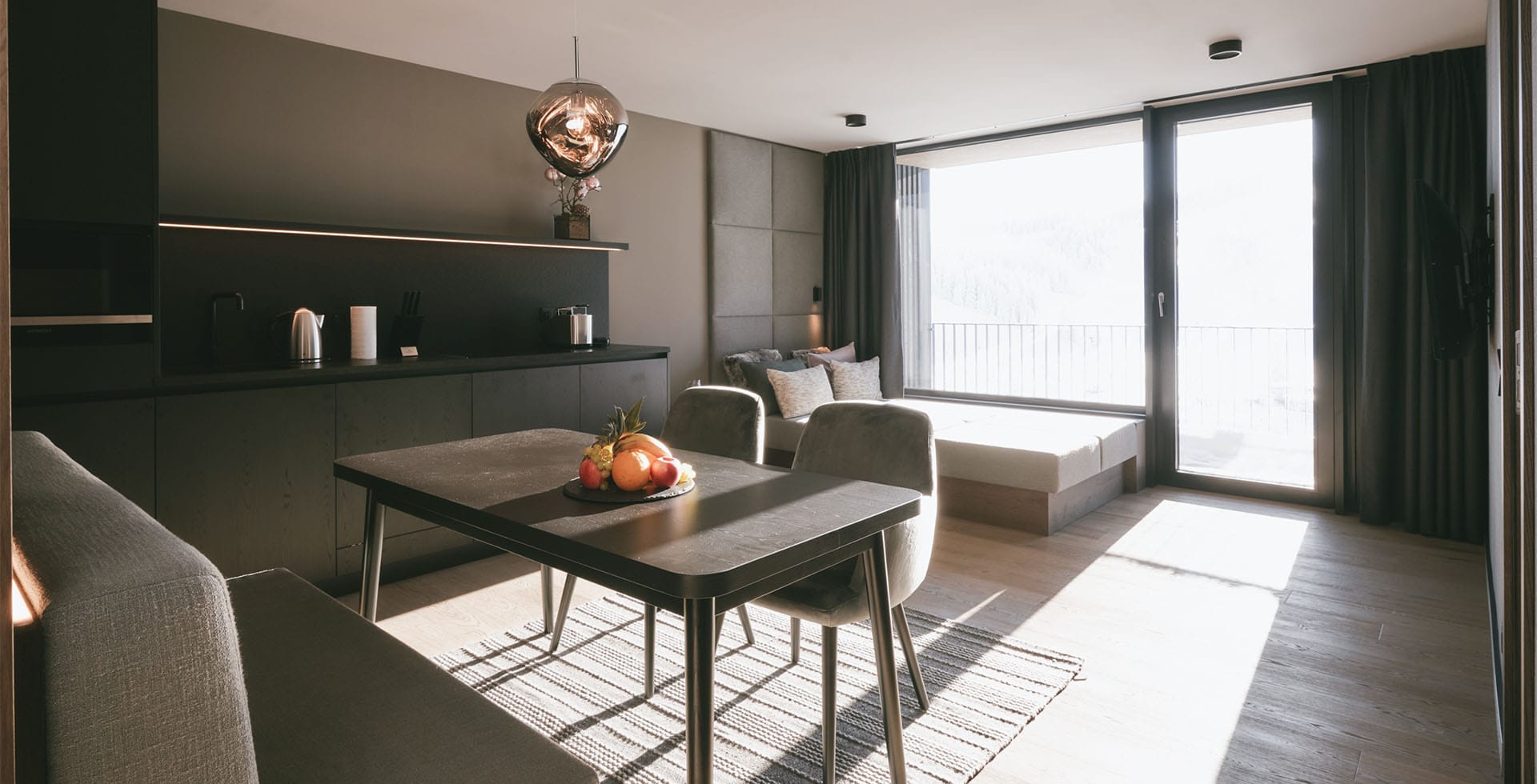 Spacious Family Suite at the TRIFORÊT alpin.resort with dining table, kitchenette, sofa and balcony view of the Alps.