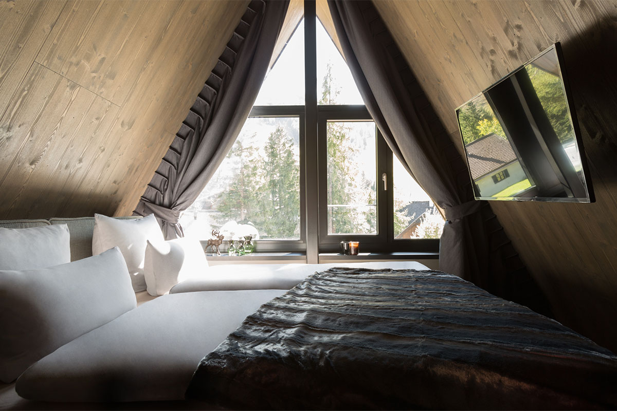 Cosy double bed beneath distinctive triangular window with forest view in Classic Chalet at TRIFORÊT alpin.resort Hinterstoder