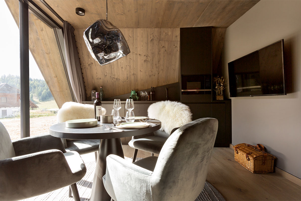 Set dining table with wine glasses velvet chairs sheepskin and kitchen area in Classic Chalet at TRIFORÊT alpin.resort Hinterstoder