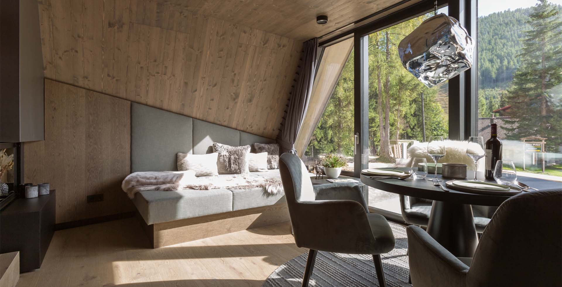 Living area in Classic Chalet with sauna at TRIFORÊT alpin.resort Hinterstoder with wood paneling bed dining table and forest view through glass front