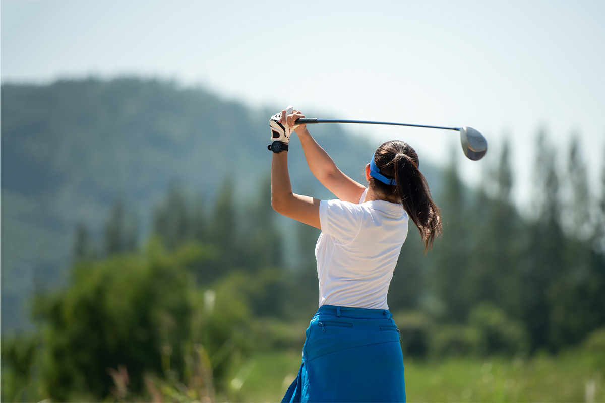 Frau spielt Golf auf einem Golfplatz mit Panoramablick auf die Alpen im Sommerurlaub im TRIFORÊT alpin.resort.