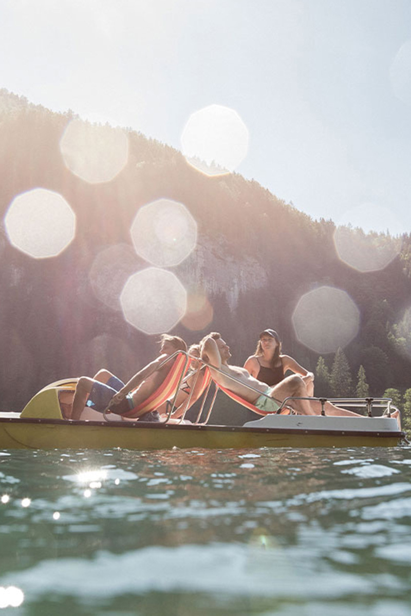 Gruppe entspannt auf Tretboot am sonnigen Bergsee im Sommerurlaub im TRIFORÊT alpin.resort in Hinterstoder.