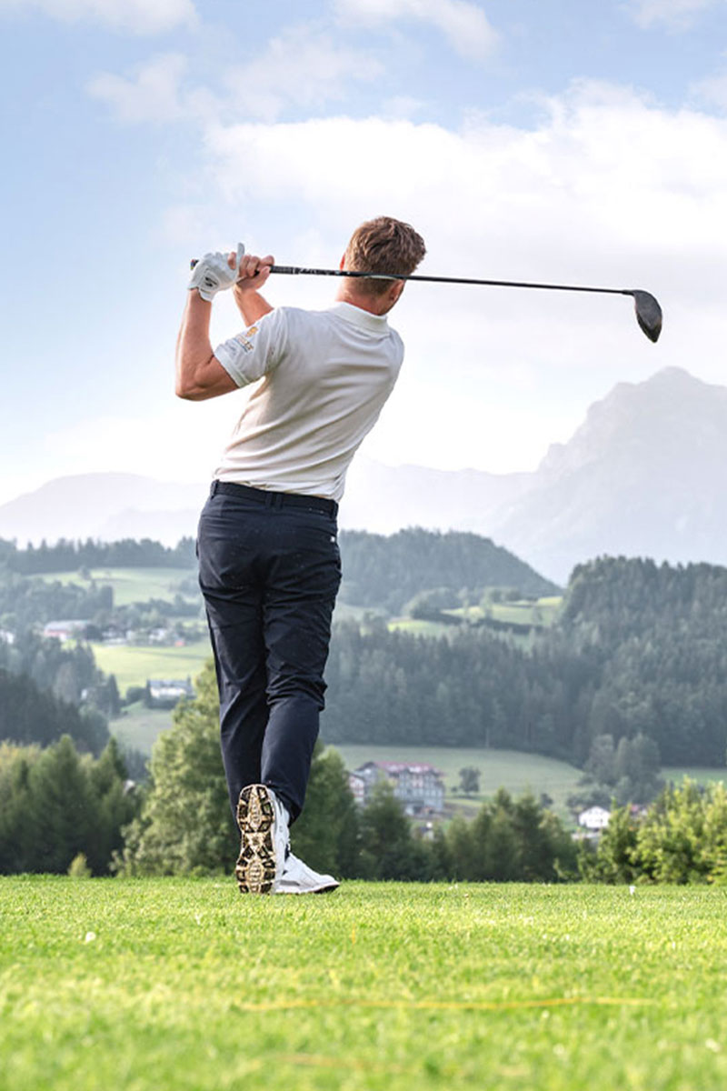 Golfer beim Abschlag mit Blick auf Berge und Täler im Sommerurlaub im TRIFORÊT alpin.resort in Hinterstoder.