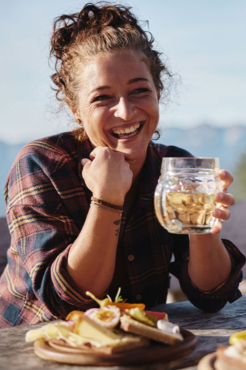 Frau genießt Bier und Brotzeit an der frischen Bergluft im Sommerurlaub im TRIFORÊT alpin.resort in Hinterstoder.
