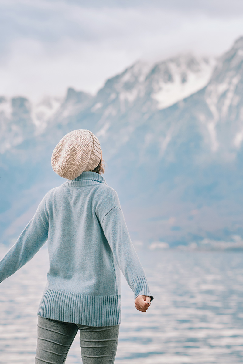 Eine Frau steht am See, umgeben von atemberaubender Berglandschaft, und genießt diesen Moment.