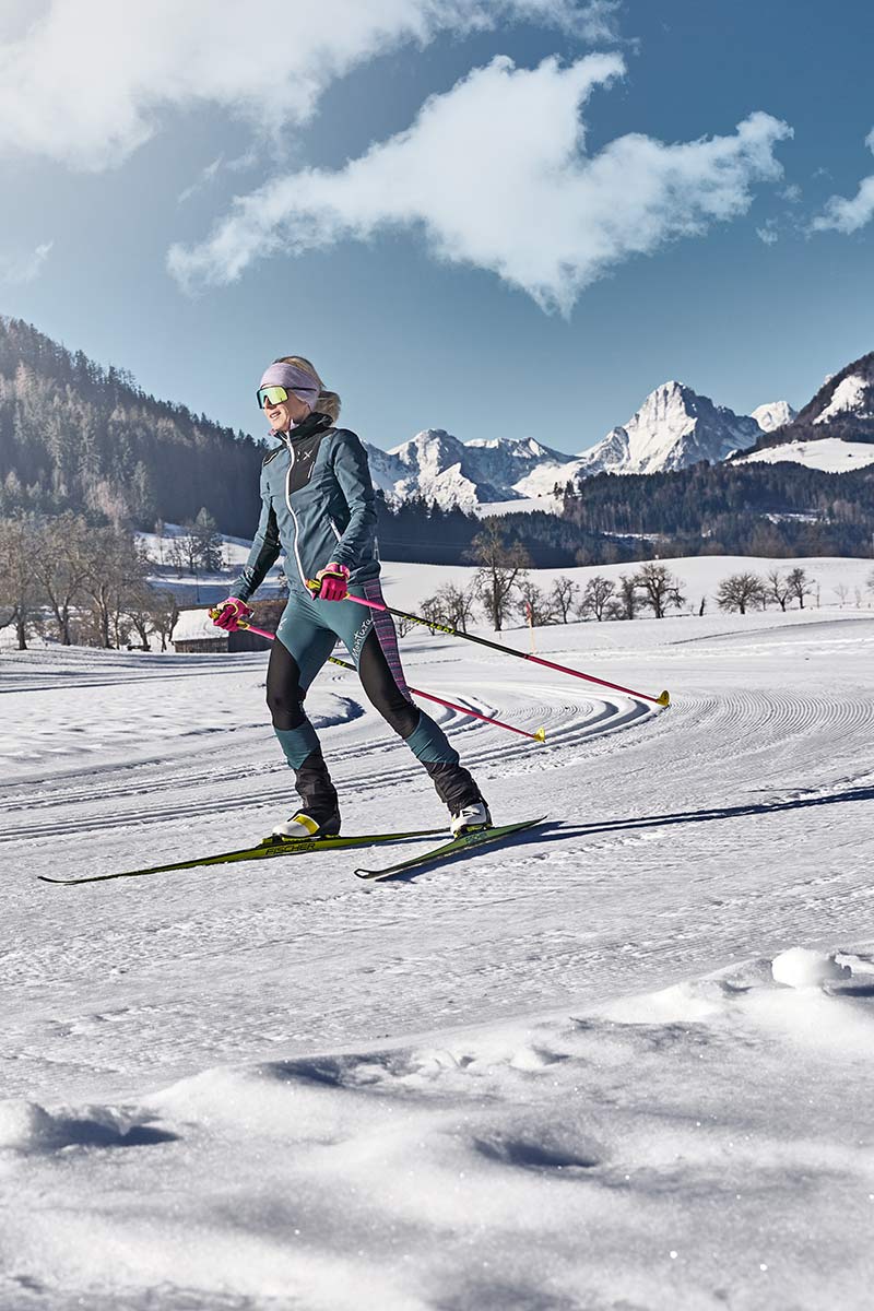 Eine Frau macht Skilanglauf im Weltcup-Skigebiet Hinterstoder und genießt die beeindruckende Berglandschaft.