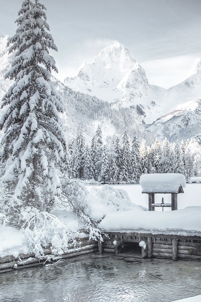 Ein eingefrorener Teich, umgeben von der schneebedeckten Berglandschaft Oberösterreichs.