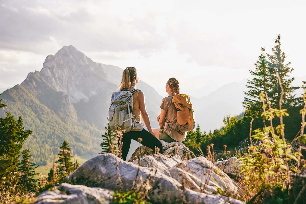 Zwei Wanderinnen mit Rucksack genießen den Blick auf die Berge bei einer Pause im im TRIFORÊT alpin.resort in Hinterstoder.
