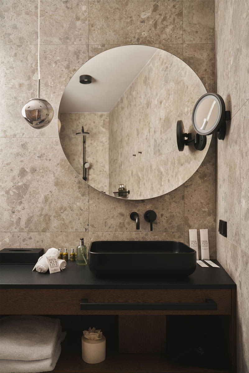 Spiegel, Stein & Stil – Ihr eleganter Waschplatz in Hinterstoder. Modernes Waschbecken mit schwarzer Armatur, großem Rundspiegel und Steinwand im TRIFORÊT alpin.resort.