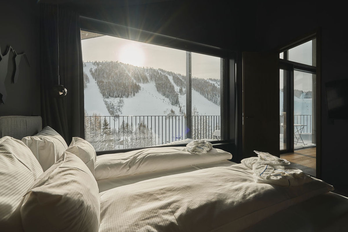 Modernes Schlafzimmer mit großen Fenstern und Blick auf verschneite Skipisten und Wald im TRIFORÊT alpin.resort in Hinterstoder.