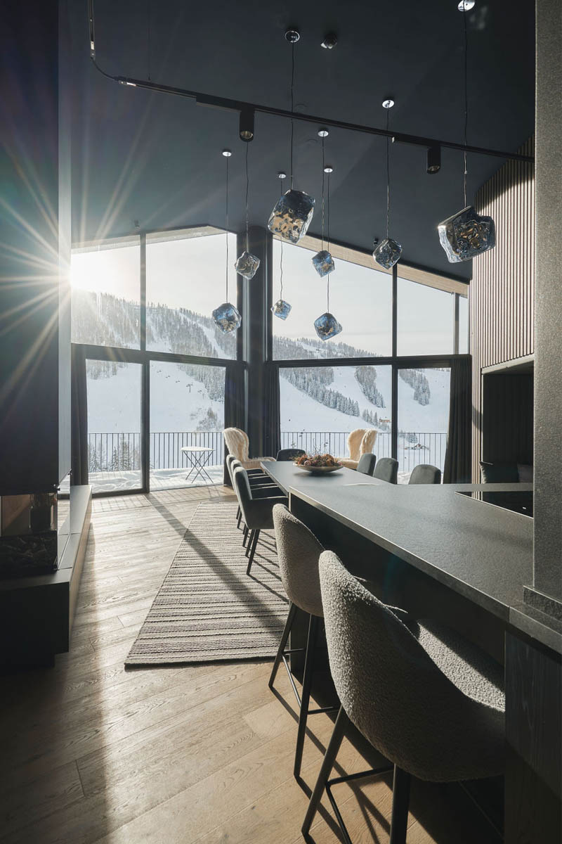 Innenaufnahme eines modernen Chalets im TRIFORÊT alpin.resort mit großem Fenster und Blick auf schneebedeckte Berge.