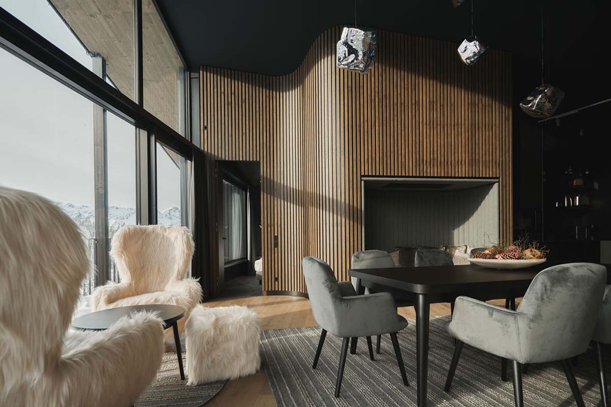 Wohn- und Essbereich im Chalet im TRIFORÊT alpin.resort mit modernen Sesseln, Esstisch und Blick durch Panoramafenster.