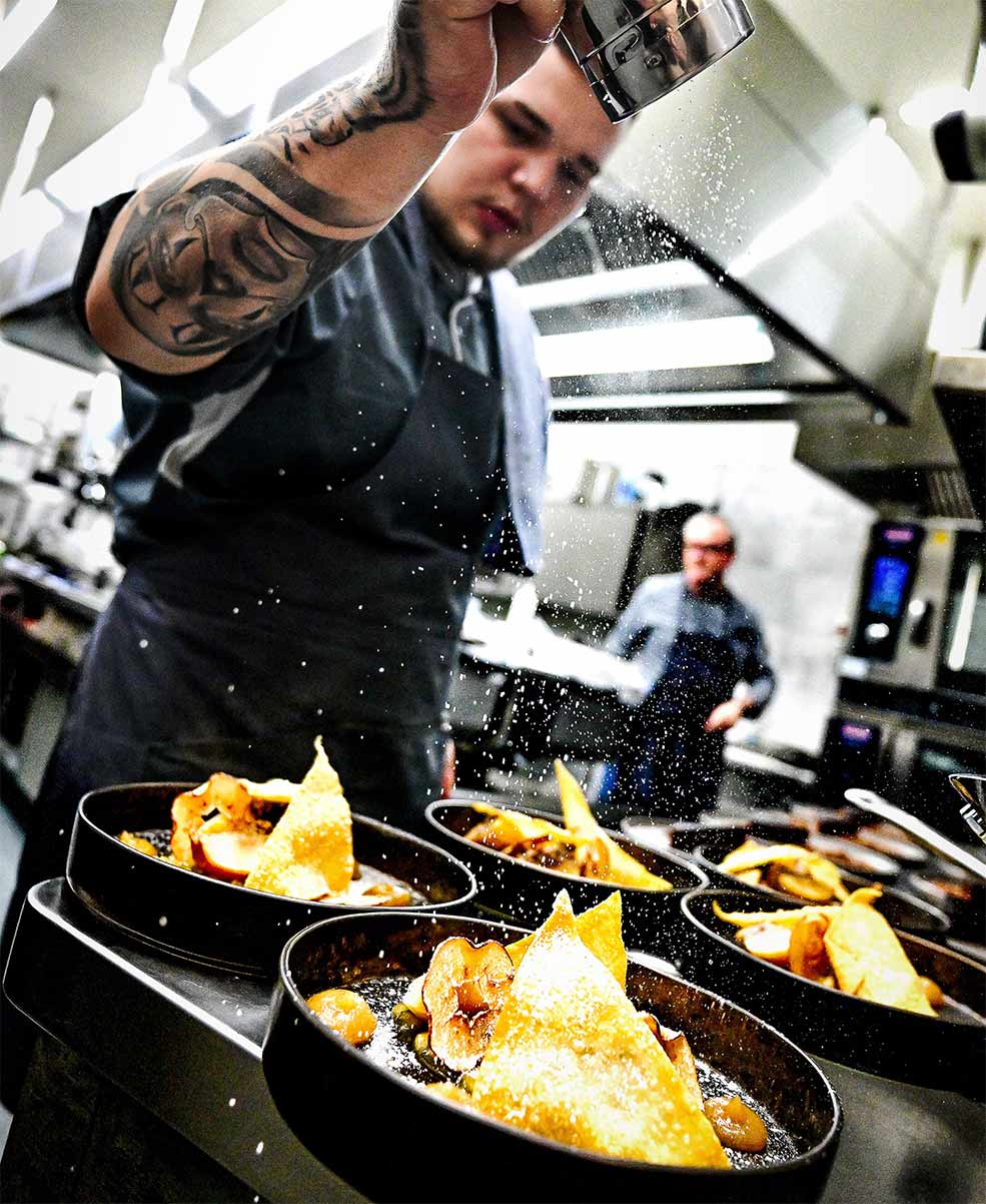 A young chef scatters precise ingredients over plates in the modern restaurant kitchen at TRIFORÊT alpin.resort.