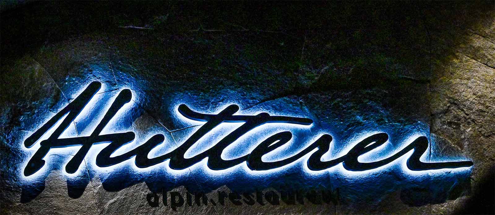 Illuminated wall logo of the Hutterer alpin. Restaurant for culinary enjoyment on vacation at TRIFORÊT alpin.resort in Hinterstoder.