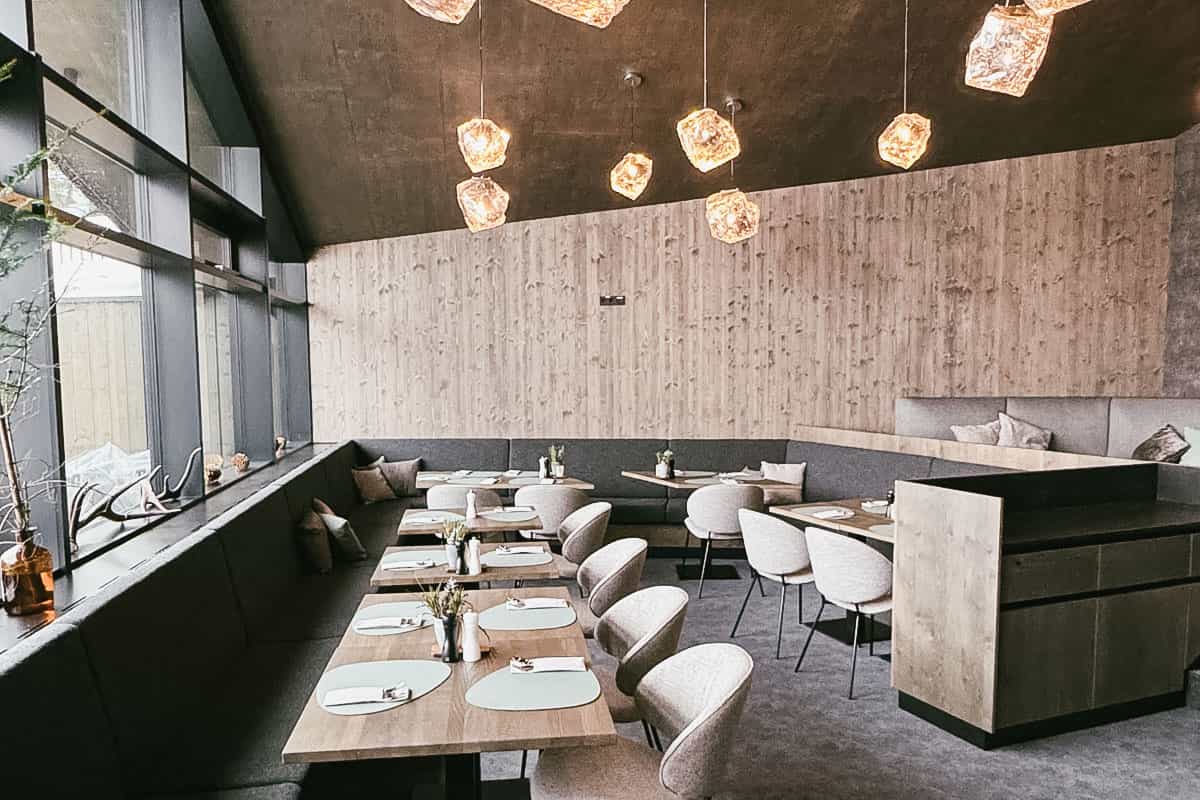 Bright interior of the Restaurant Hutterer in the TRIFORÊT alpin.resort with wooden décor, windows and elegantly laid tables.