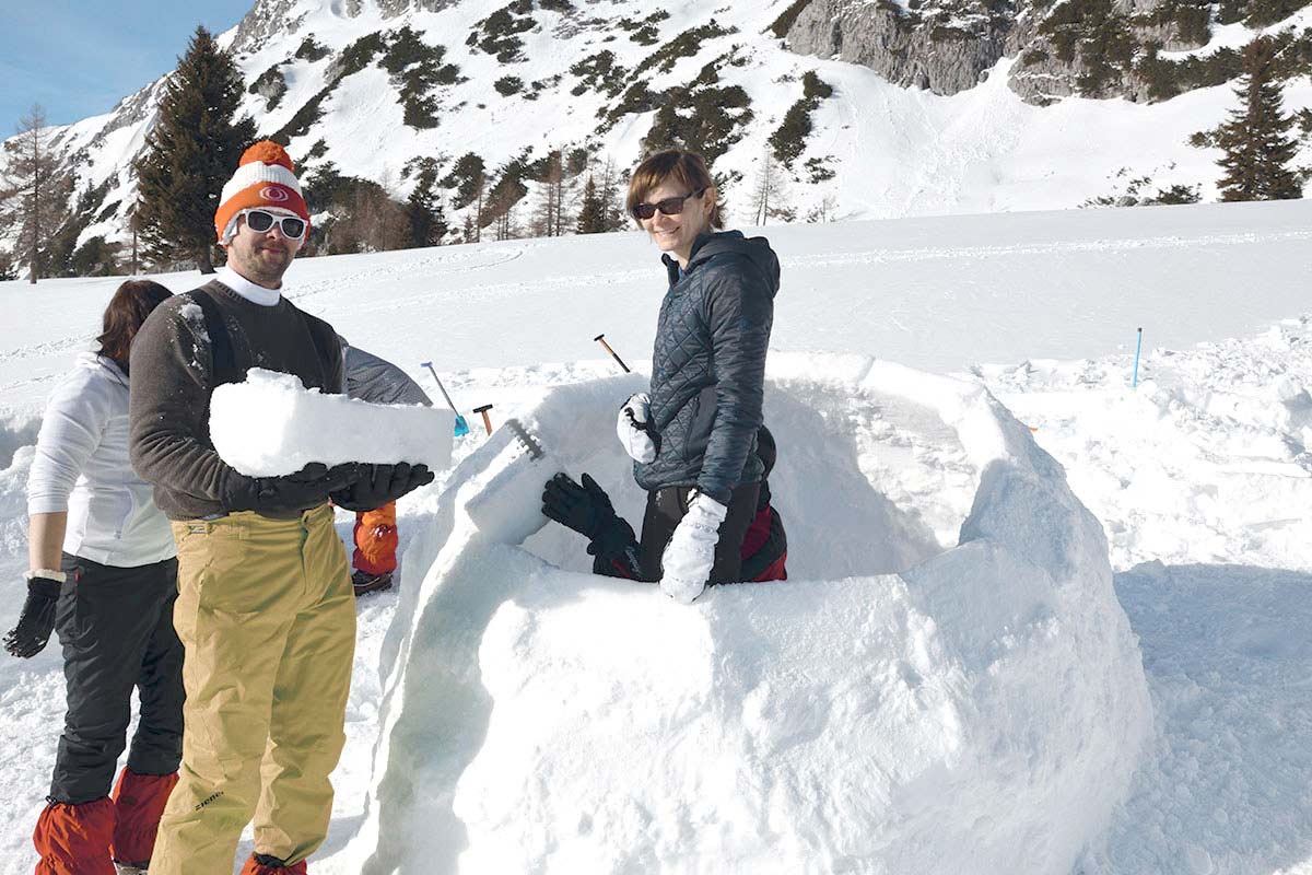 Group on an incentive activity in the snow: building an igloo with a mountain panorama in the background on vacation at TRIFORÊT alpin.resort.